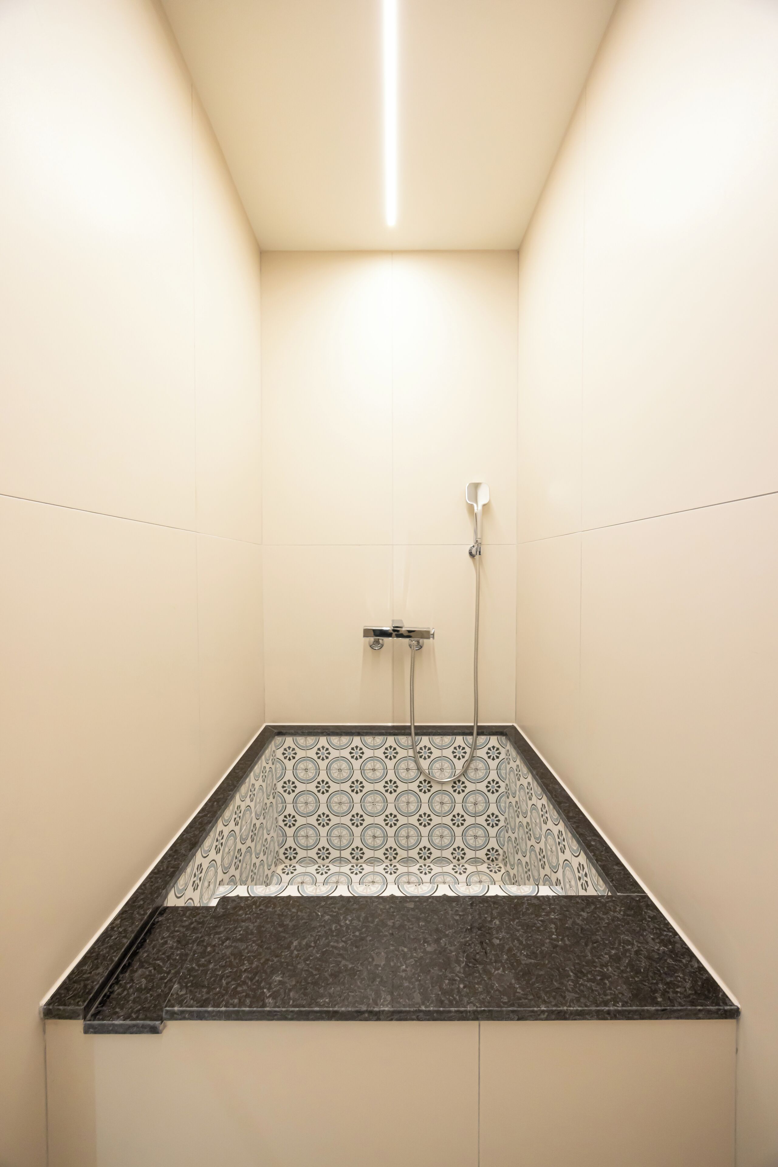 Um espaço de chuveiro pequeno e fechado, com piso estampado e um chuveiro.