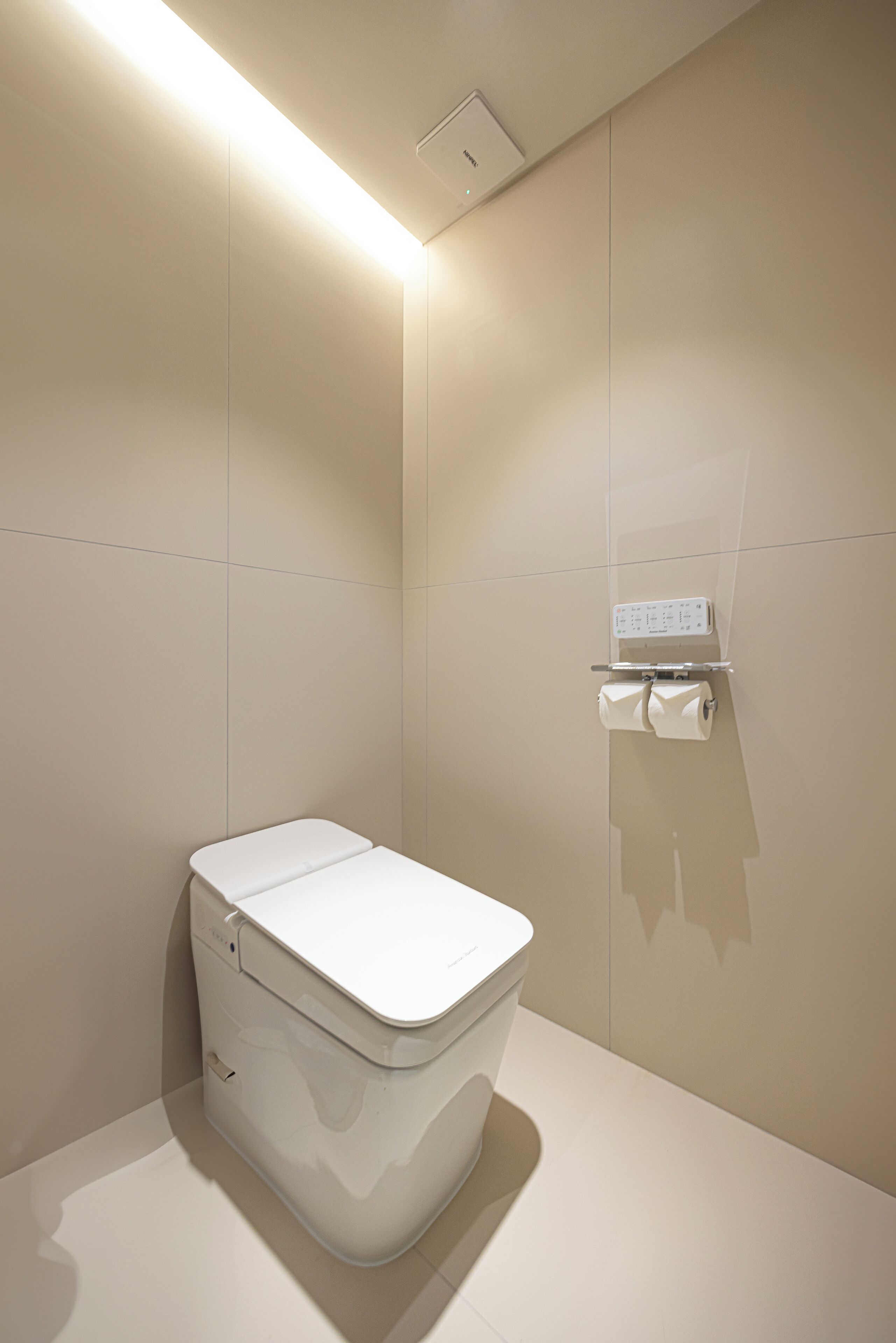 A modern bathroom with a white toilet, a wall-mounted toilet paper holder, and a light fixture on the ceiling.