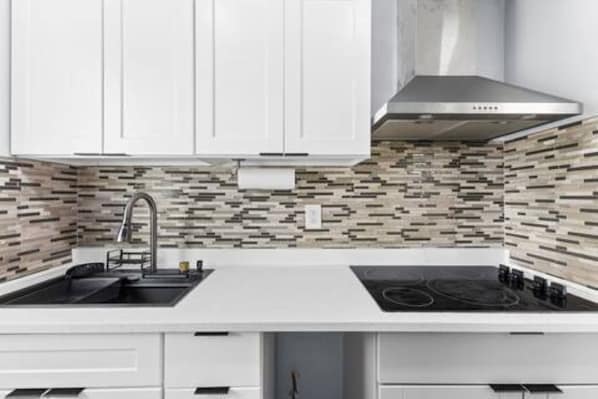 A modern kitchen with white cabinetry, a black sink, and a stainless steel range hood.