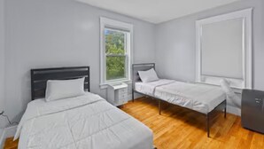 A bedroom with two single beds, a nightstand, a desk, and a window. - Roger William 2nd Floor- 3 Bedroom apartment ALL included- Long Term (Providence)