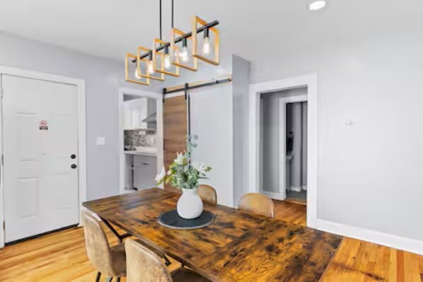 A dining area with a wooden table, chairs, a vase with flowers, and a modern pendant light fixture.