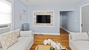 A living room with a flat-screen TV mounted on a wall, two sofas, a wooden floor, and a radiator. - Roger William 2nd Floor- 3 Bedroom apartment ALL included- Long Term (Providence)