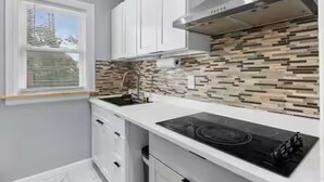 A kitchen with white cabinets, a black stove, and a patterned backsplash. - Roger William 2nd Floor- 3 Bedroom apartment ALL included- Long Term (Providence)