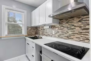 Una cucina con mobili bianchi, un piano cottura nero e un rivestimento a parete decorato.