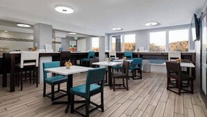 A modern restaurant with multiple tables and chairs, a kitchen area, and large windows offering a view. - Motorcycle Inn (Kodak)