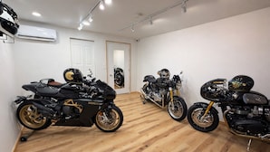 A room with three motorcycles, wooden flooring, white walls, and an air conditioning unit. - Motorcycle Inn (Kodak)