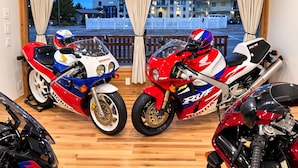 Two motorcycles parked indoors with a view of a building outside. - Motorcycle Inn (Kodak)
