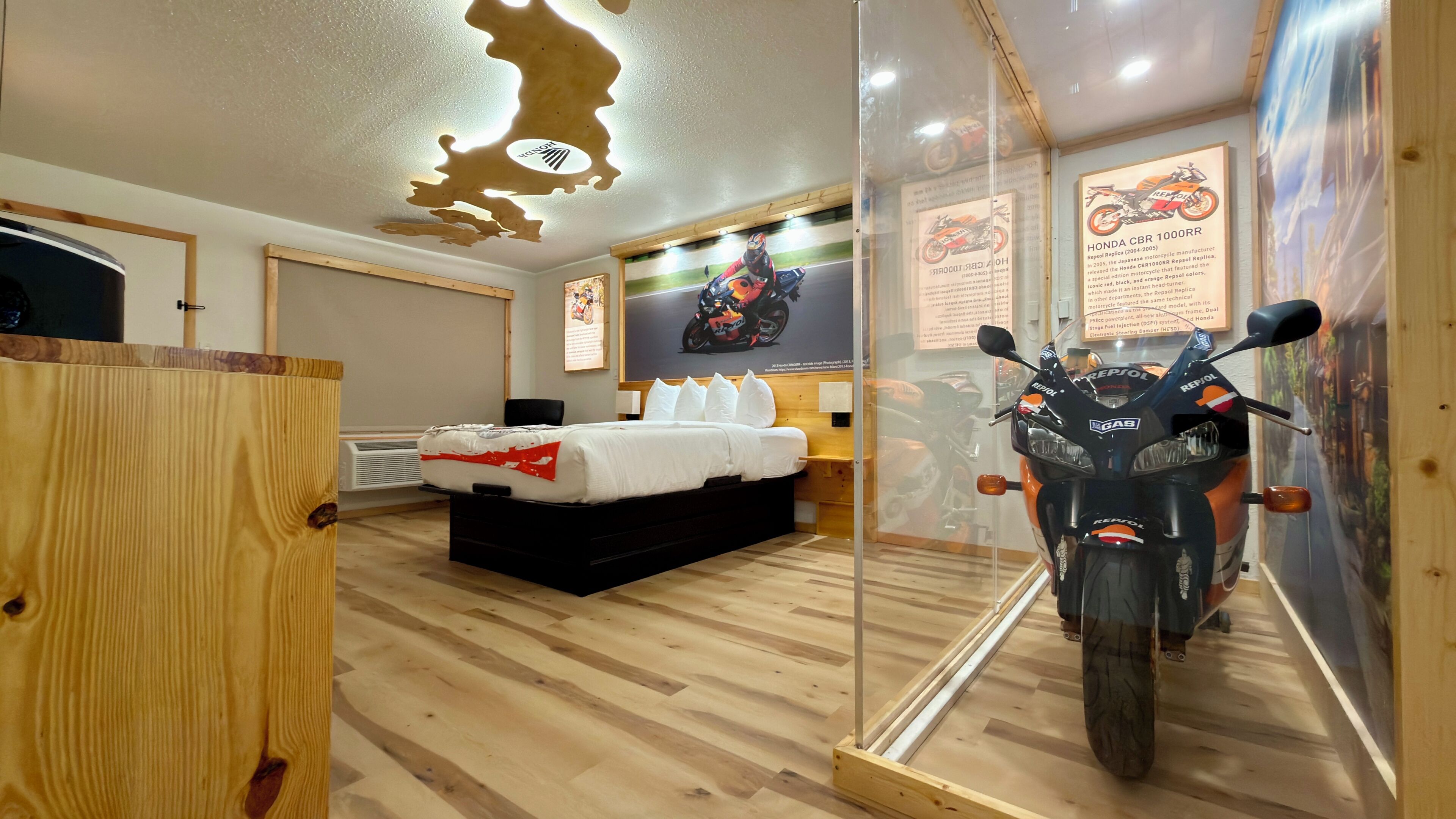 A hotel room with a bed, a motorcycle in a glass display, and posters on the wall.