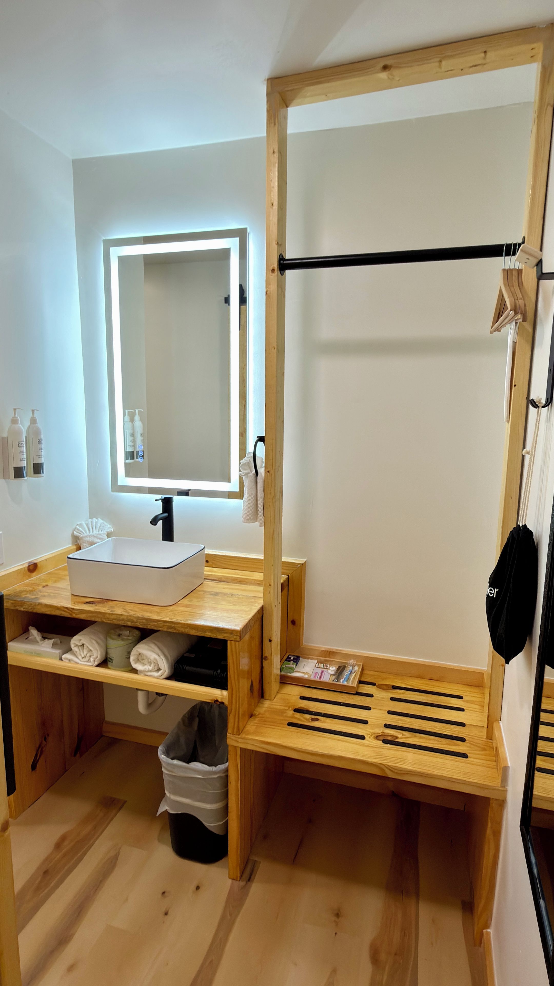 A bathroom with a wooden vanity, a mirror, a towel rack, and a shelf with toiletries.