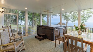 Un espacio exterior techado con jacuzzi, sillas de madera, una mesa y vistas al océano.