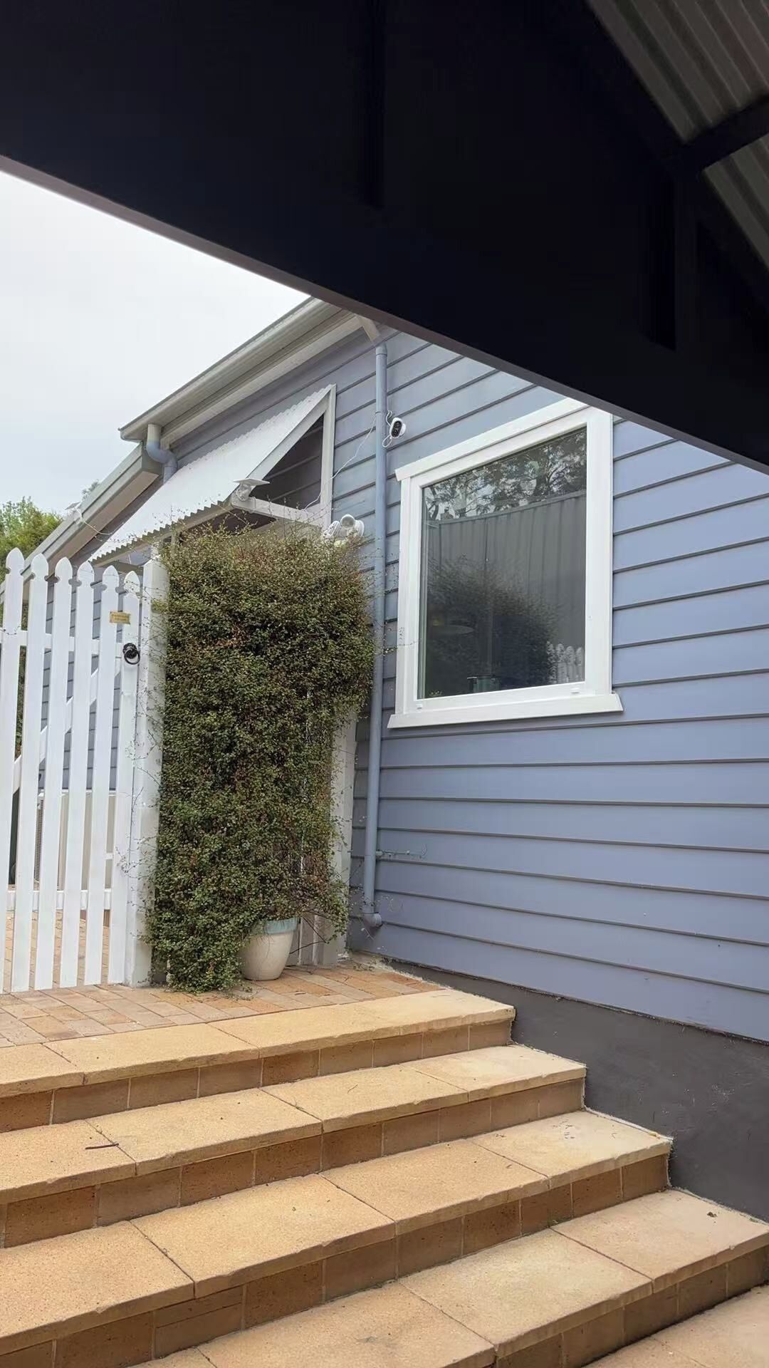 A house with a white picket fence, a potted plant, and a window.