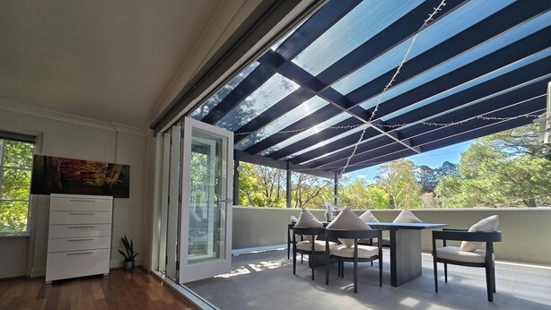 A modern room with a wooden floor, a dining area with a table and chairs, a large window with a view of trees, and a sliding glass door.