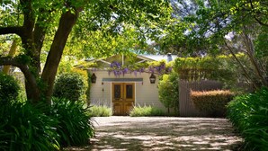 Une maison avec une porte en bois, entourée d’une végétation luxuriante et accessible par un chemin de gravier.