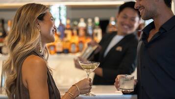 A bar area with a bartender and two guests holding drinks.