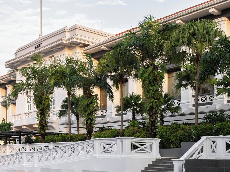 A multi-story hotel with a white facade, palm trees, and a white bridge.