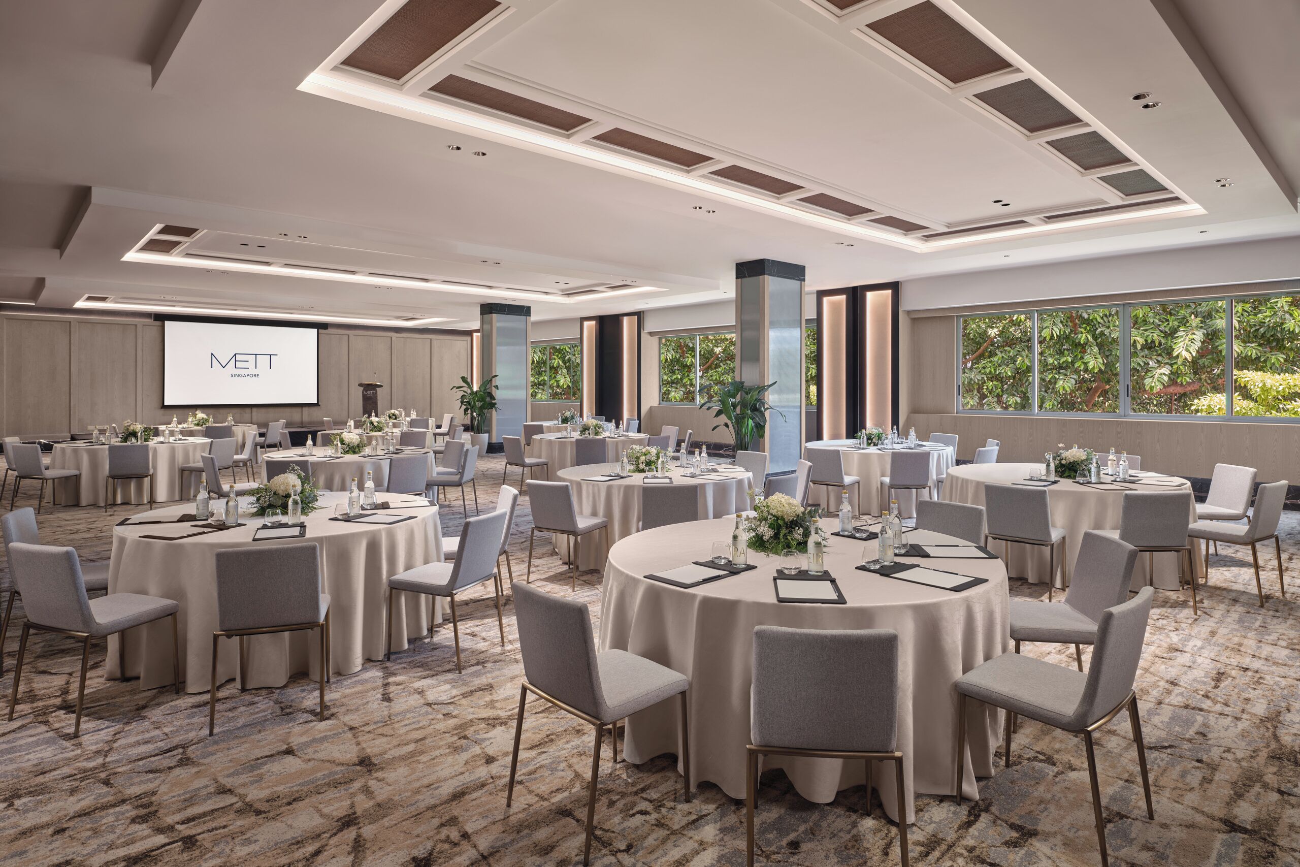 Un salón de conferencias con varias mesas redondas, sillas y una pantalla grande.
