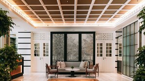 A spacious room with a wooden floor, a round table, and two chairs. There is a large window with a view of trees, and a white cabinet with glass doors. - METT Singapore (Singapore)