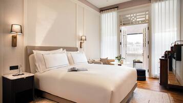 Habitación de hotel amplia con una cama grande, lámparas de noche, una mesita con una planta y vistas a la ciudad a través de una ventana.