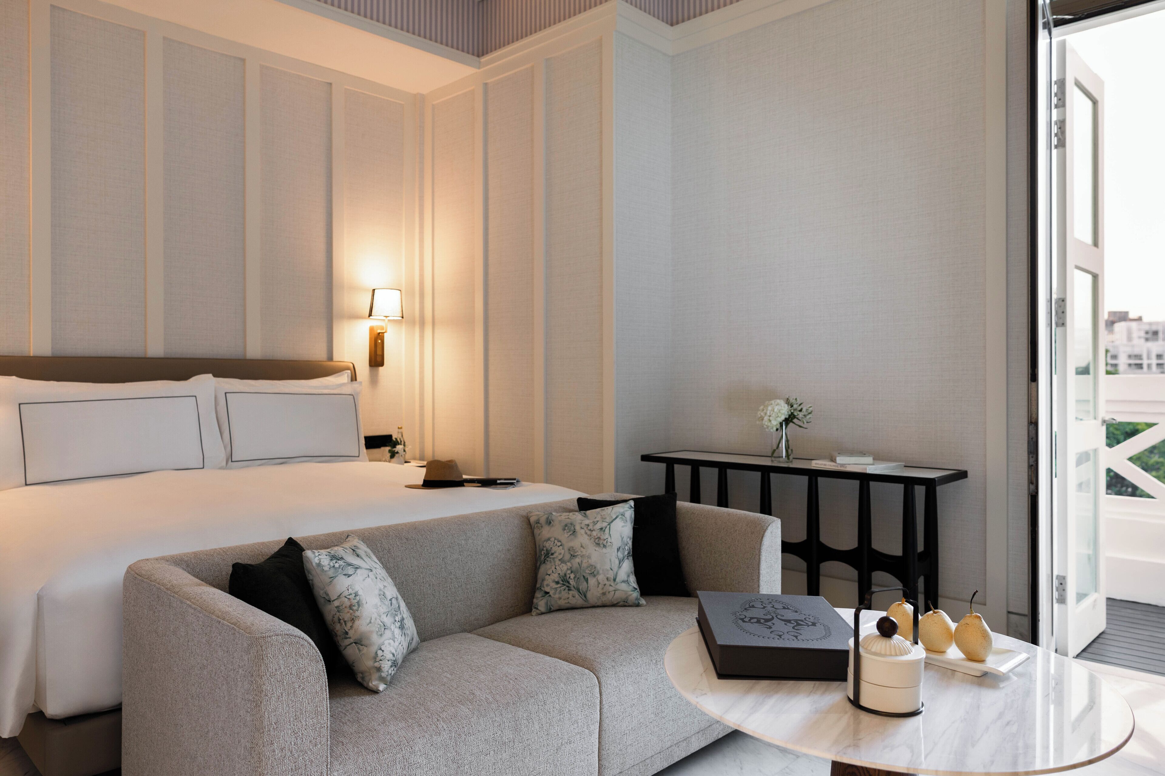 A hotel room with a bed, a sofa, a table with decorative items, and a view of the outside.