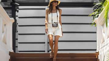 Una persona baja por una escalera de madera, con una correa de cámara, vestida con un conjunto blanco y un sombrero de paja.
