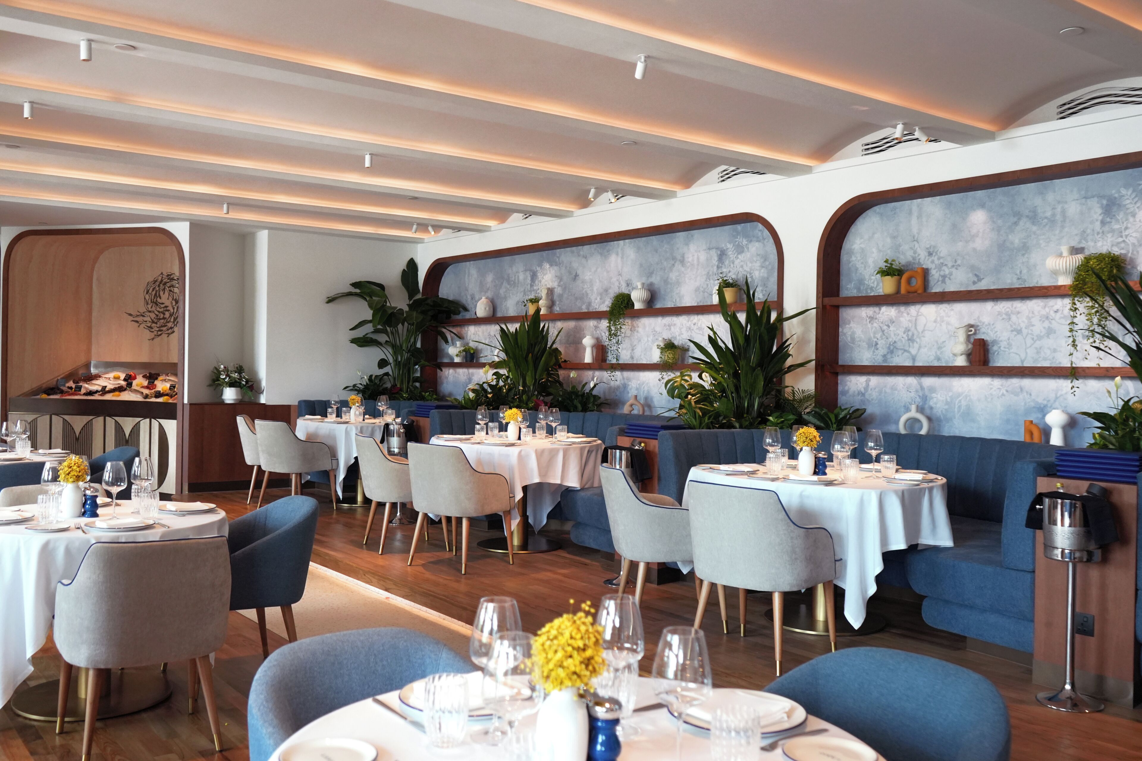 Un restaurant avec des tables rondes, des chaises et des étagères ornées de plantes.