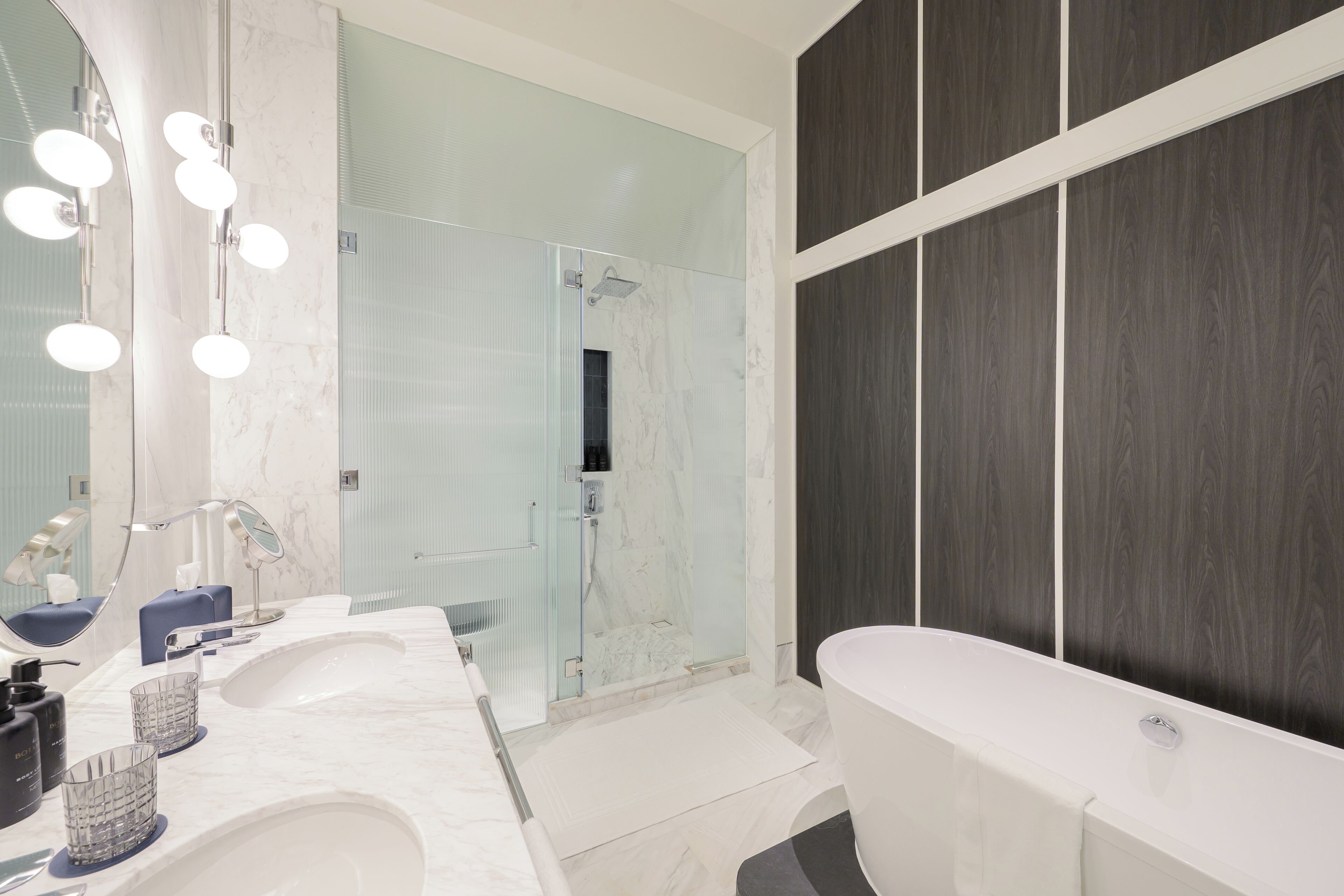Un baño moderno con una bañera grande, una ducha con cerramiento de vidrio y un tocador con espejo e iluminación.