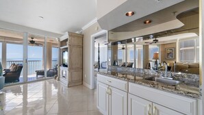 Un'ampia cucina con una grande isola, una porta scorrevole in vetro che dà su un balcone e vista sull'oceano.