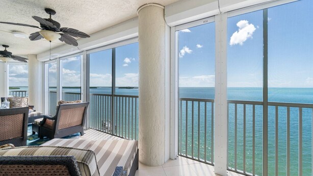Un ampio balcone con vista sull'oceano, arredato con sedie in vimini e una tovaglia a righe.