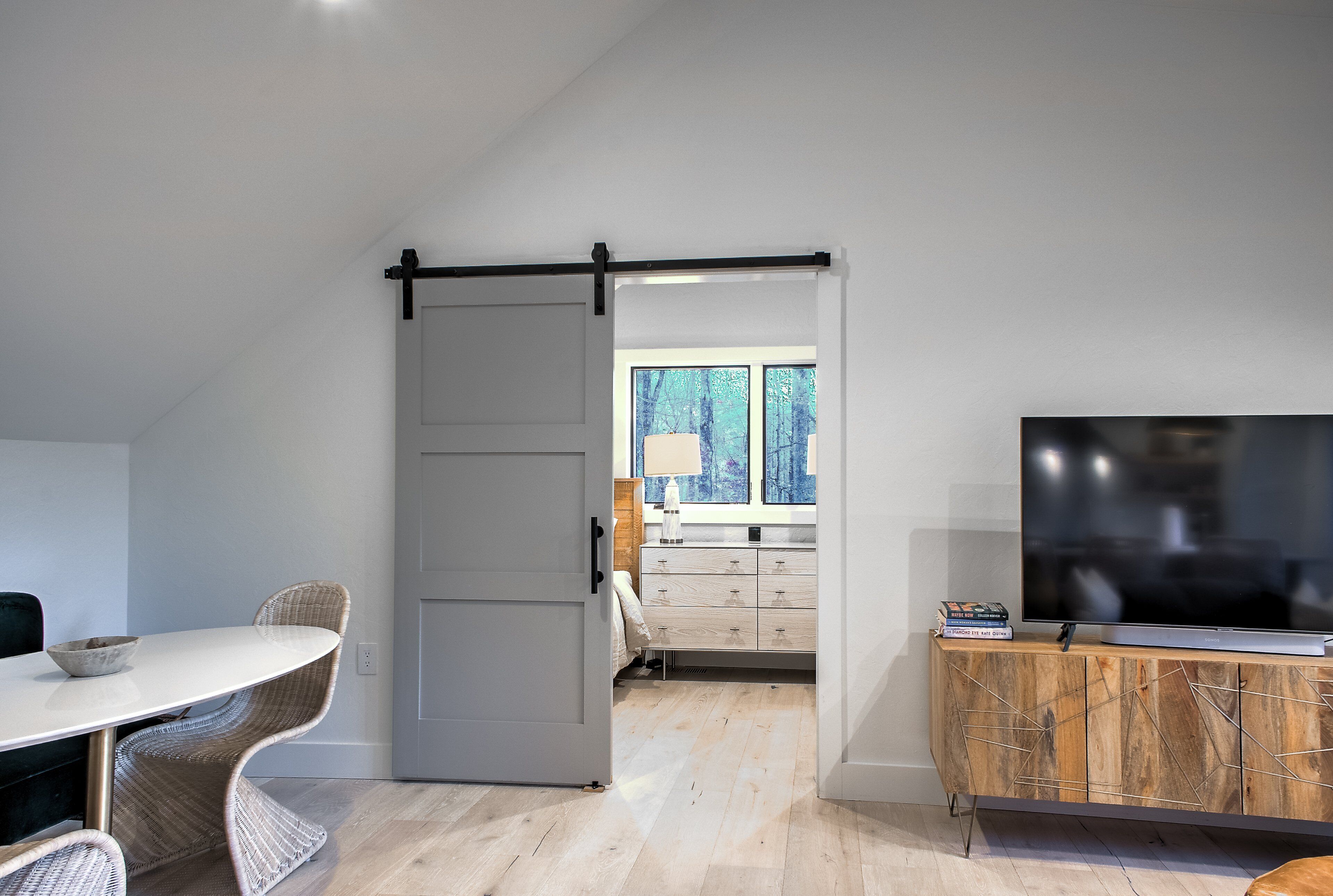 A modern living space with a dining area, a sliding door leading to a bedroom, and a TV on a wooden cabinet.