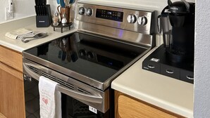 A kitchen with wooden cabinets, a stainless steel microwave, an oven, a coffee maker, and a set of knives. - Buck Creek Condos C103 2 Bedroom Condo (Avon)