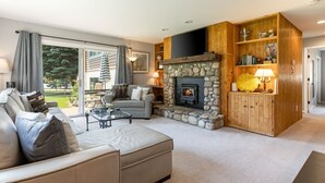 A cozy living room with a stone fireplace, a sofa, a coffee table, and a bookshelf. - Buck Creek Condos C103 2 Bedroom Condo (Avon)