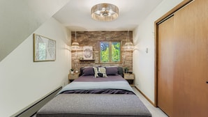 Un dormitorio con una cama, un armario de madera, una pared de ladrillo y una ventana que da a árboles.