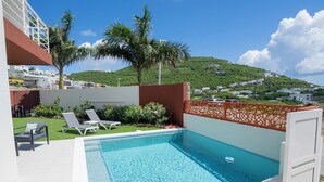 A swimming pool with lounge chairs, a view of a hillside, and a building in the background.