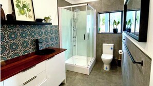 Une salle de bain moderne dotée d’une douche à parois de verre, de toilettes blanches et d’un lavabo avec un plan de travail en bois.