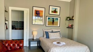 Une chambre à coucher avec un lit, une table de chevet, un canapé en cuir rouge et des œuvres d’art accrochées au mur.