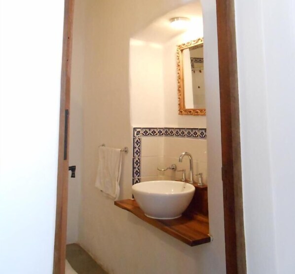 Een badkamer met een wit wastafelmeubel, een houten plank, een spiegel en een betegelde achterwand.