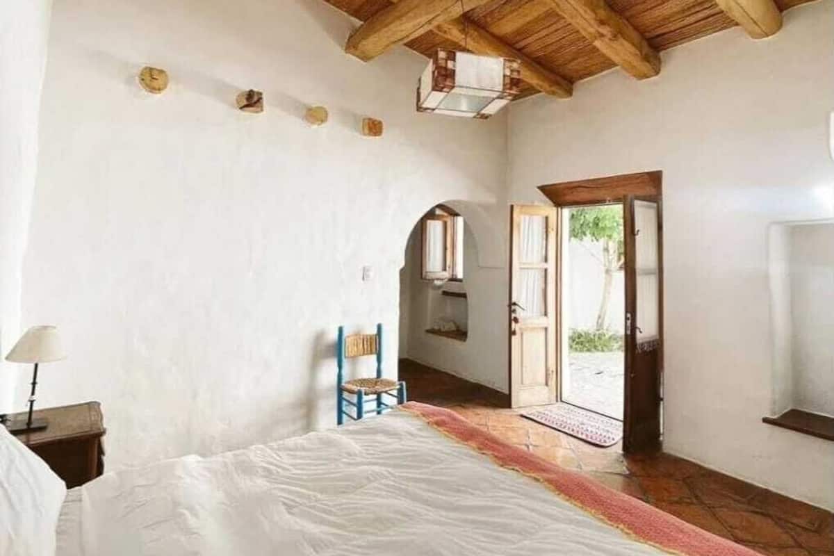 A bedroom with a wooden ceiling, a bed, a nightstand, a lamp, and a window.