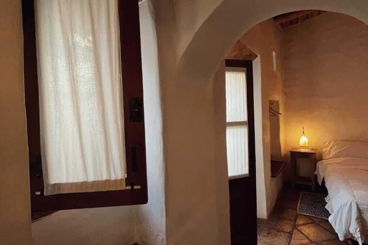 A narrow hallway leading to a bedroom with a bed, a nightstand, and a lamp.