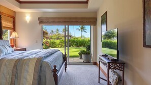 A bedroom with a bed, a TV, and a view of a garden through a sliding door. - Spacious Family Retreat! Ocean View Sunsets + Pool, Spa & Beach Club (Waimea)
