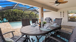 Uma área de refeições ao ar livre com vista para a piscina, mobiliário de vime e um ventilador de teto.