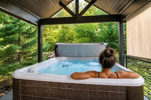 A hot tub with a wooden deck and a view of trees.