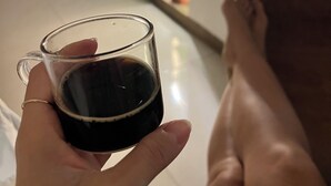 A person holding a glass of dark liquid, possibly coffee, in a room with a white floor and a window with a view of greenery outside. - Monet apartment-studio. Tranquility, style and location.  (Santa Marta)