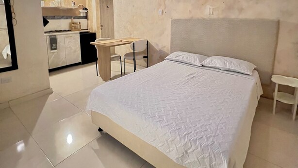 A modern bedroom with a large bed, a small desk, and a kitchenette in the background. - Monet apartment-studio. Tranquility, style and location.  (Santa Marta)