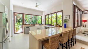 A modern kitchen with a central island, large windows, and a view of greenery. - Villa Tres Delfines Private Pool And Family Fun Puerto Aventuras (Puerto Aventuras)