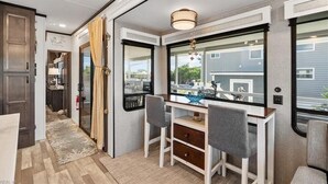Ein kompaktes Wohnmobil-Interieur mit einer Küchenzeile, einer Essecke mit zwei Stühlen und einem großen Fenster mit Aussicht.