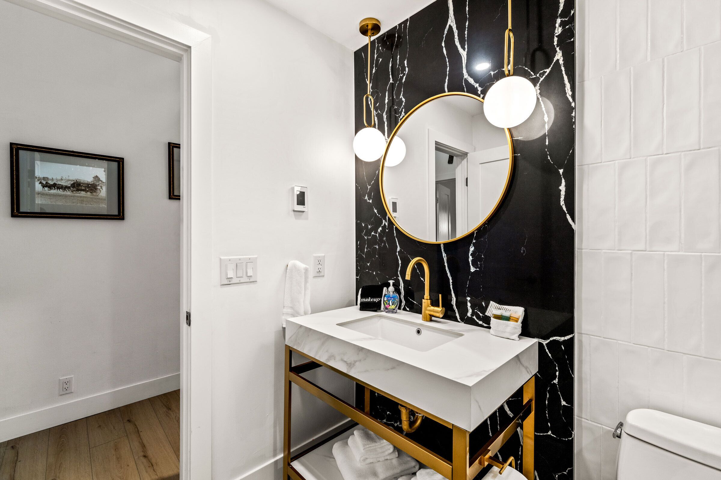 A modern bathroom with a white sink, gold fixtures, and a black marble backsplash.