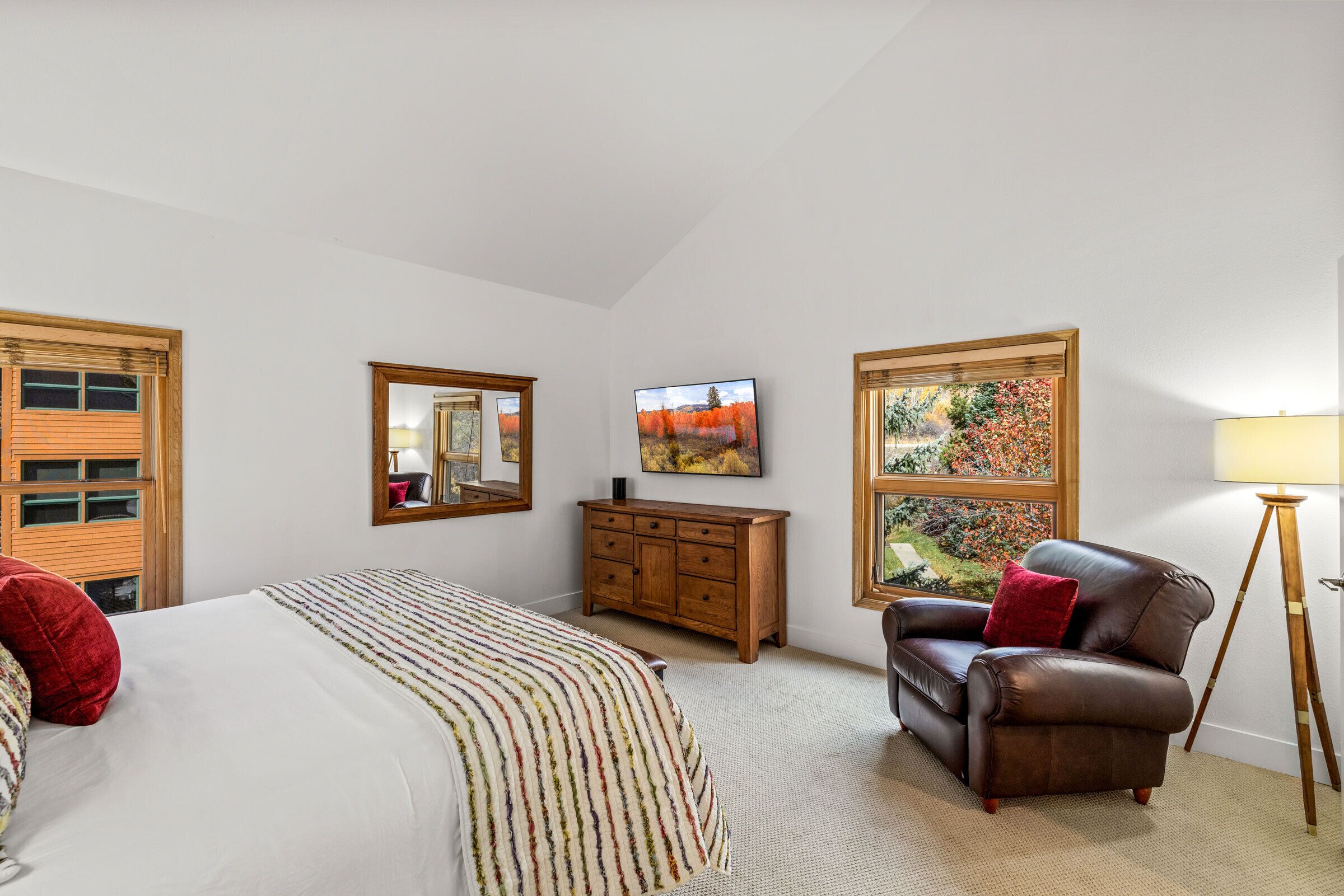 Une chambre à coucher comprenant un lit, une commode, une chaise, une lampe, un miroir et un tableau accroché au mur.