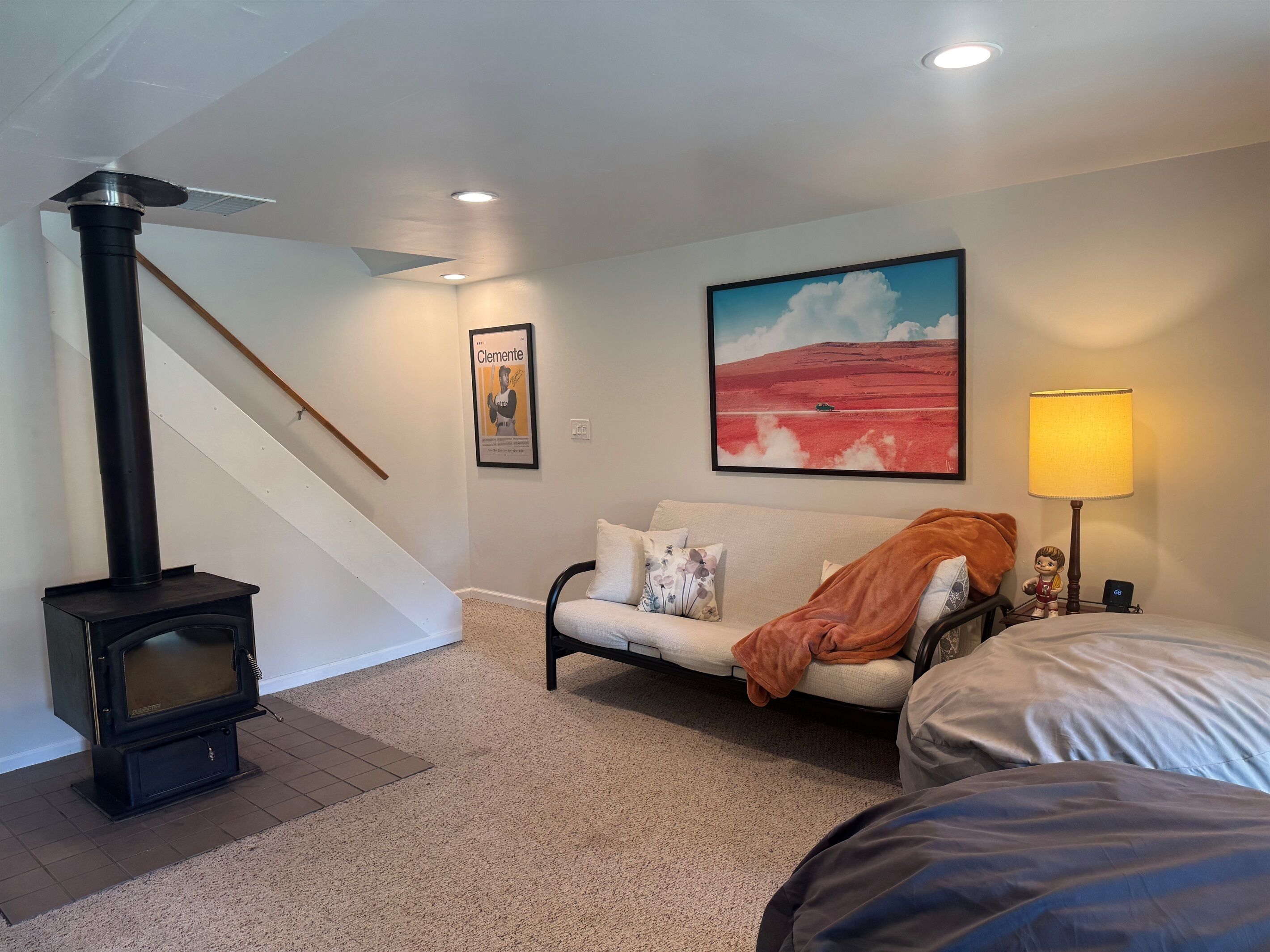 Une pièce chaleureuse avec une cheminée, un canapé, un lit, une lampe et un tableau au mur.