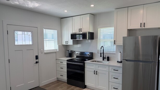 A modern kitchen with white cabinets, stainless steel appliances, and a black stove.