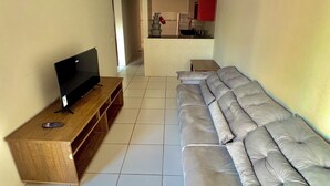 Ein Wohnzimmer mit Fernseher auf einem Holzboden, einer Couch und einer Küche im Hintergrund.